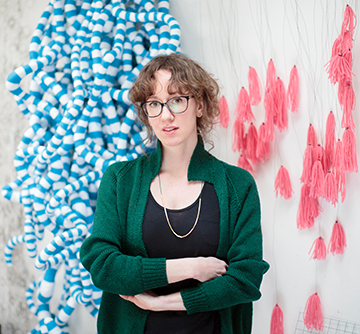 A photograph of artist Anna Ray standing  in front of fabric pink sculpture