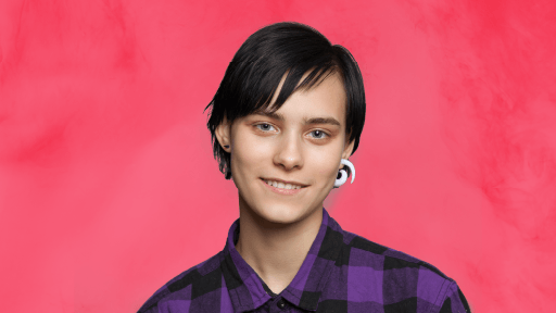 A person with a white looped earing smiles to camera against a pink background