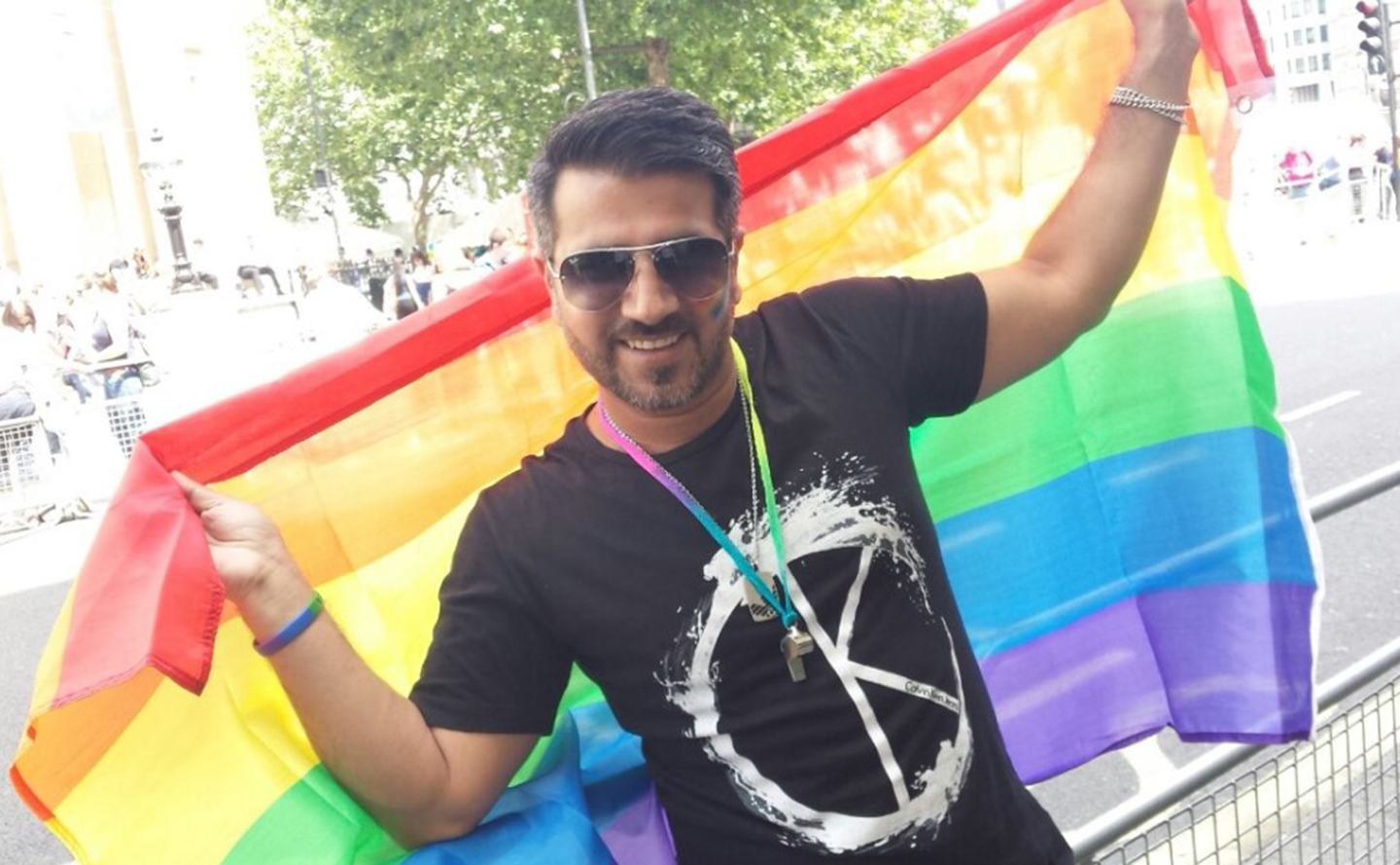 Mohammed leans against a railing, holding the LGBT rainbow flag