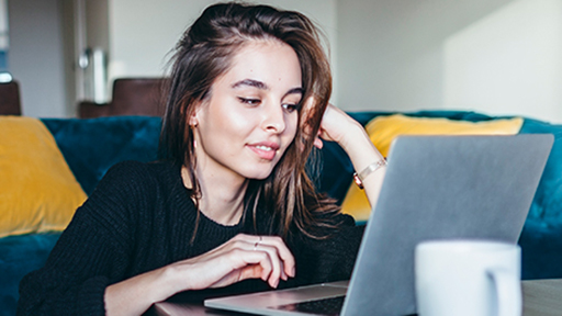 a woman sits on the floor, working on a laptop on the coffee table.