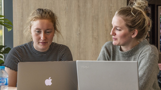 two students work on their laptops in a cafe