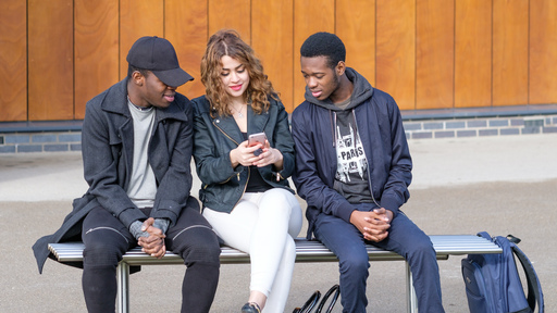 Students sitting on a bench looking at a mobile together