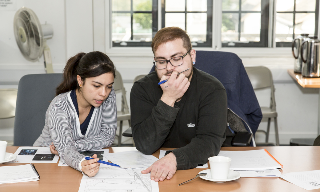 Two students sitting in a classroom analysing maps and images