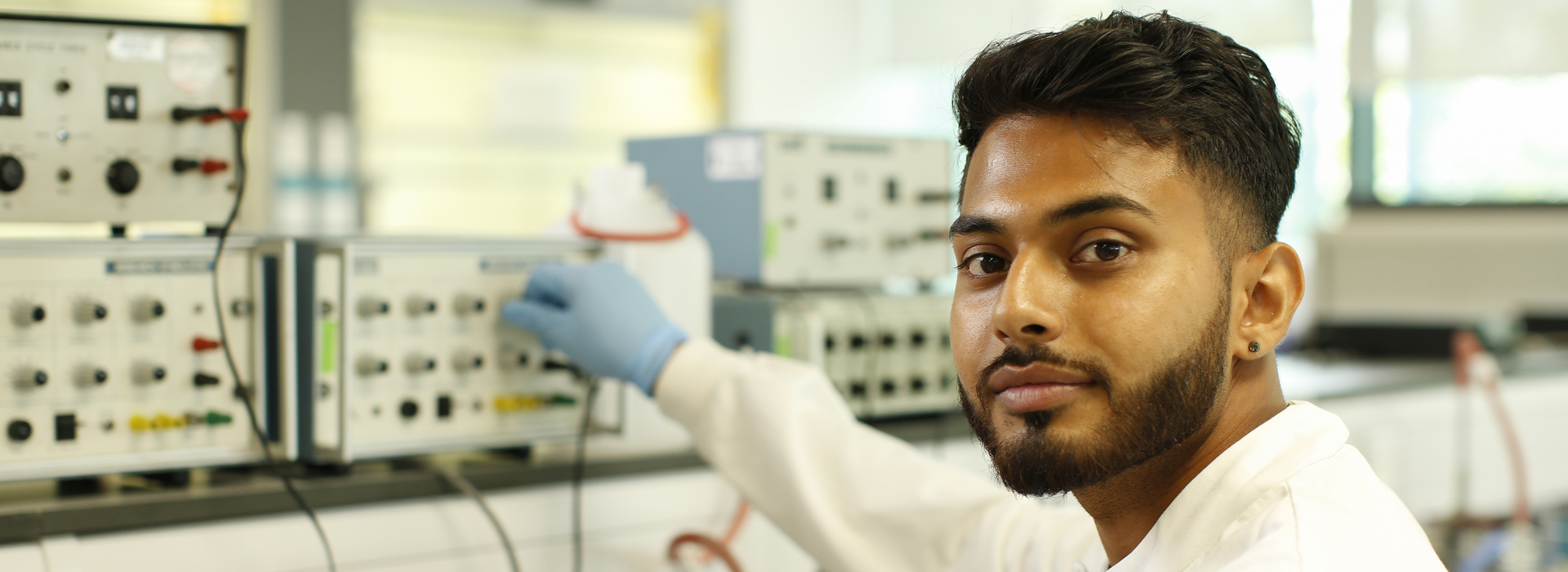 a male student operating a dial whilst smiling at the camera in our lab