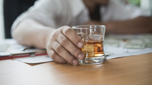 Hand holding glass of whiskey on a table