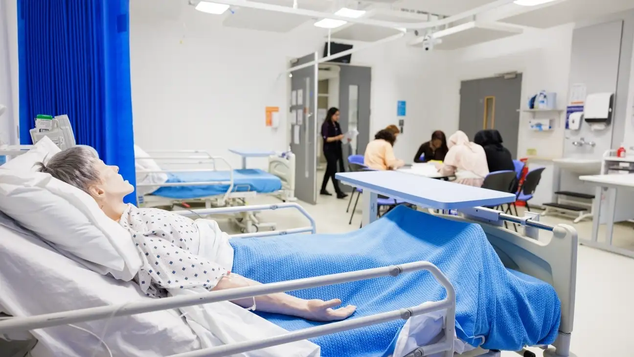 A group of student sitting round a table with a dummy laying in a hospital bed