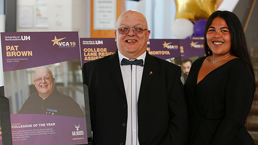 Pat Brown smiles by a poster which says 'colleague of the year'