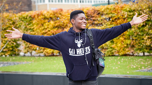 a man spreads out his arms and smiles in a Herts hoodie