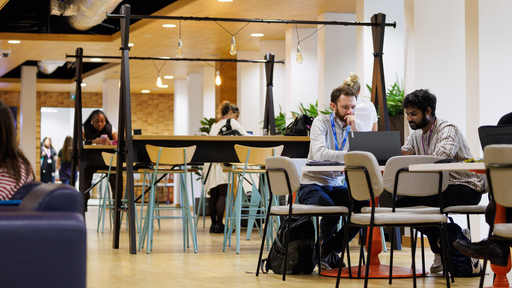 People sat at tables working on laptops in a communal space