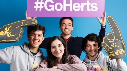 Group of four smiling students with Go Herts banner