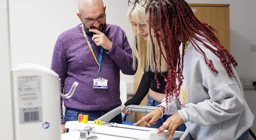 Two students looking at a bit of equipment with a lecturer