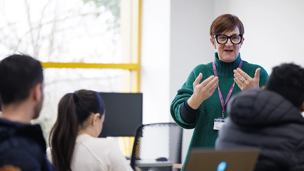 A lecturer talking to their class with hand raised