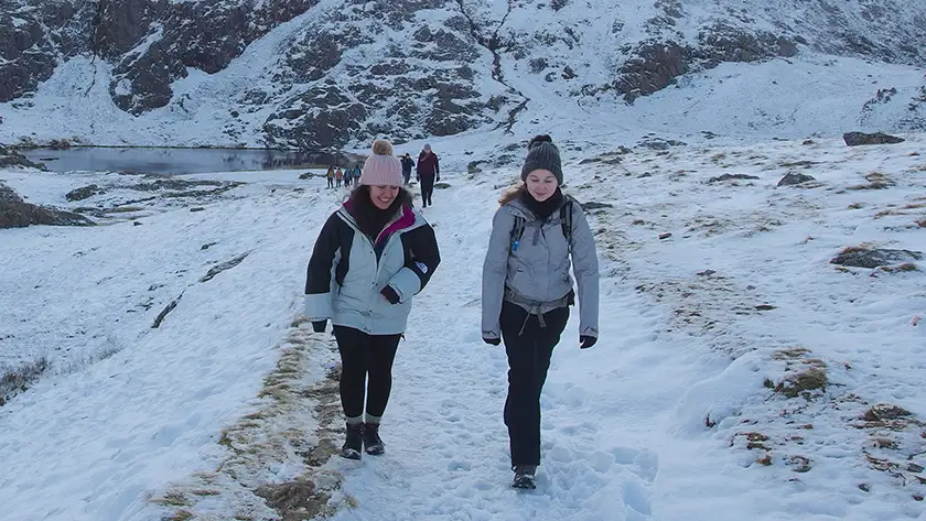 Two students walking through a mountainside with snow on it