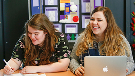 two students sit in a row with their laptops