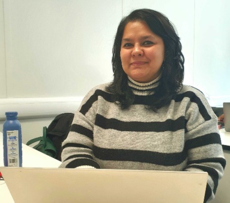 A smiling student sitting at a desk with an open laptop in front of her