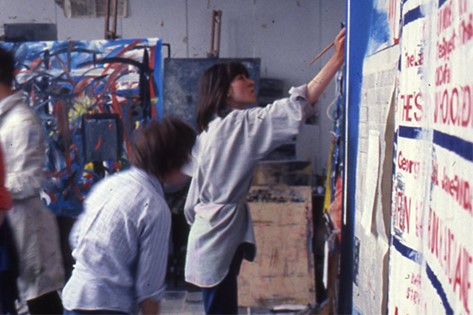 View of a woman painting in an art studio with another figure in front of her