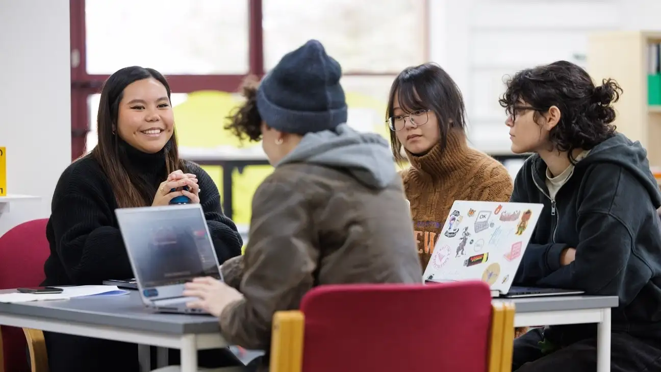 A group of students round a table smiling and talking