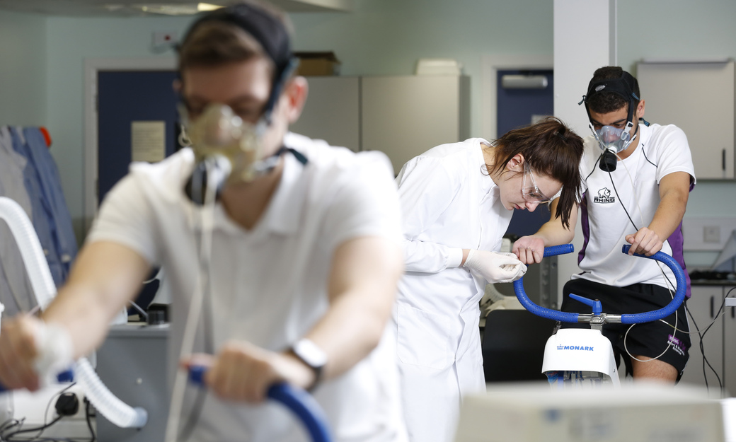 Two students on exercise bikes with breathing apparatus, with one student having blood taken