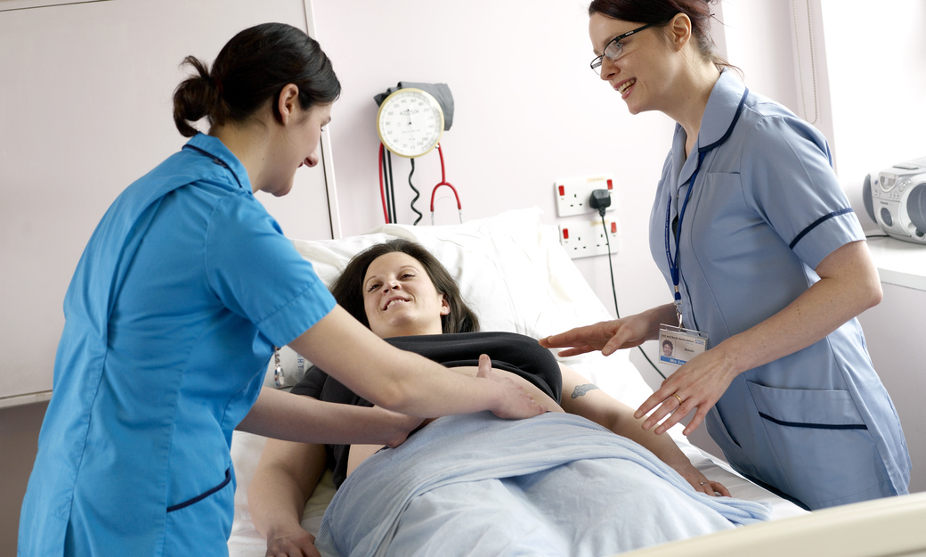two student midwives checking on a pregnant patient in a bed
