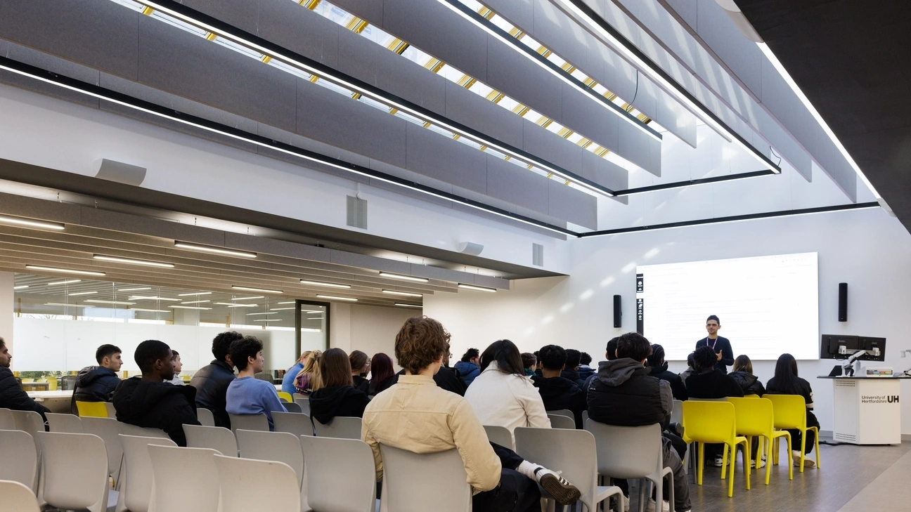 A lecturer talking to their class with hand raised