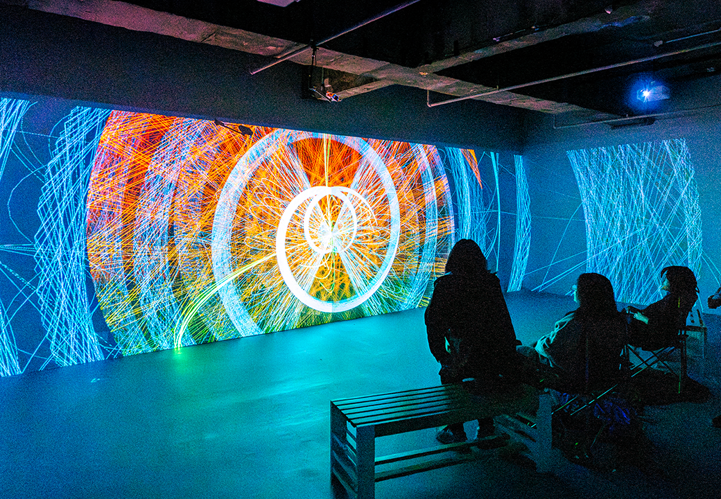 People watching a large screen displaying intricate patterns and colours