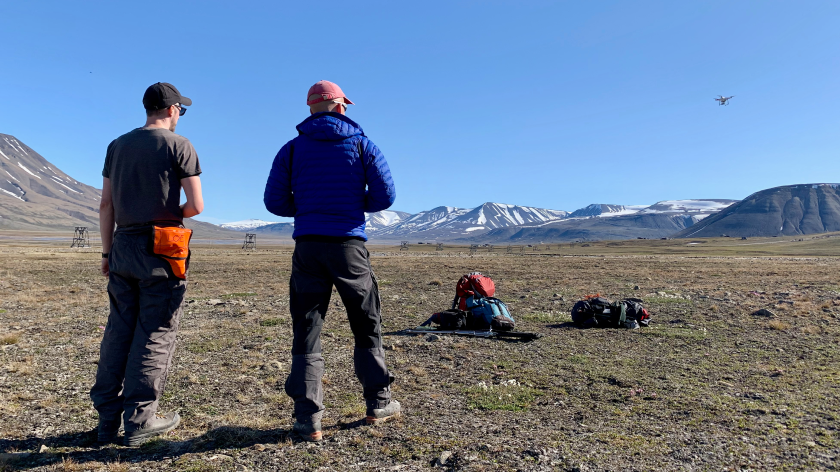 Two people standing in open ground in front of mountains