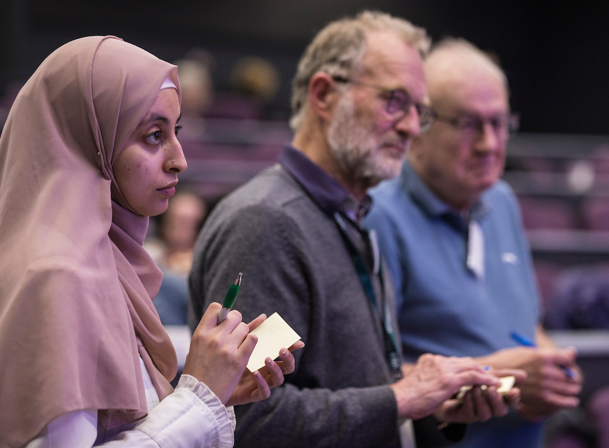 Two white man and one woman with a hijab making notes on notebooks