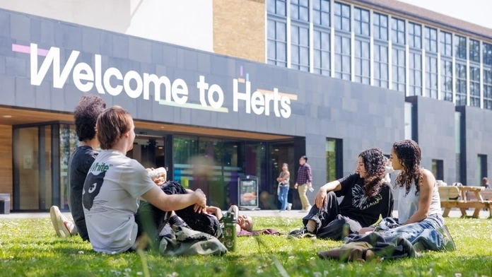 Students sitting outside Hertfordshire University on a sunny day smiling