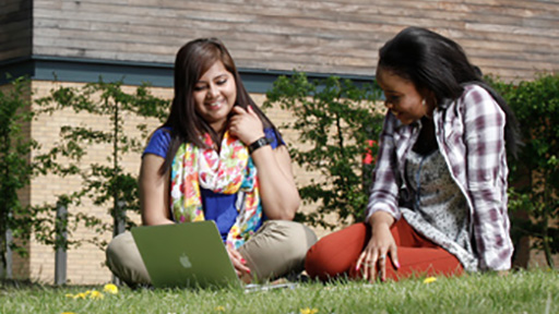 Two students sitting outside under tree