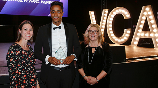 Three people stand in front of the stage, smiling with an award