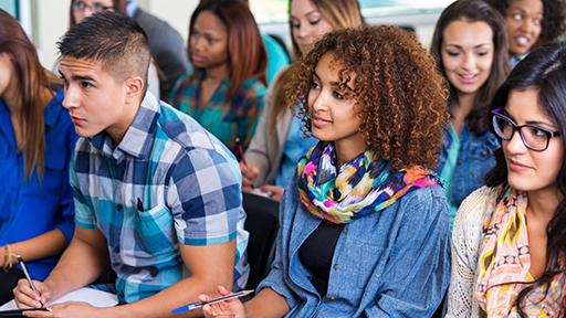 a group of teenagers sit listening with a pen and paper in hand