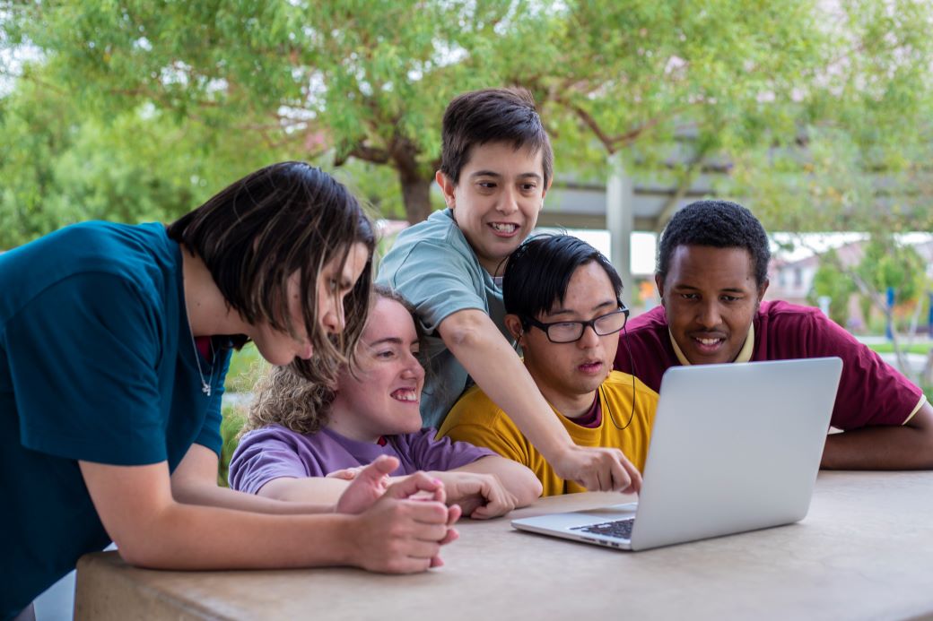 a group of additional need patients around a laptop with a nursing student pointing at the screen. 