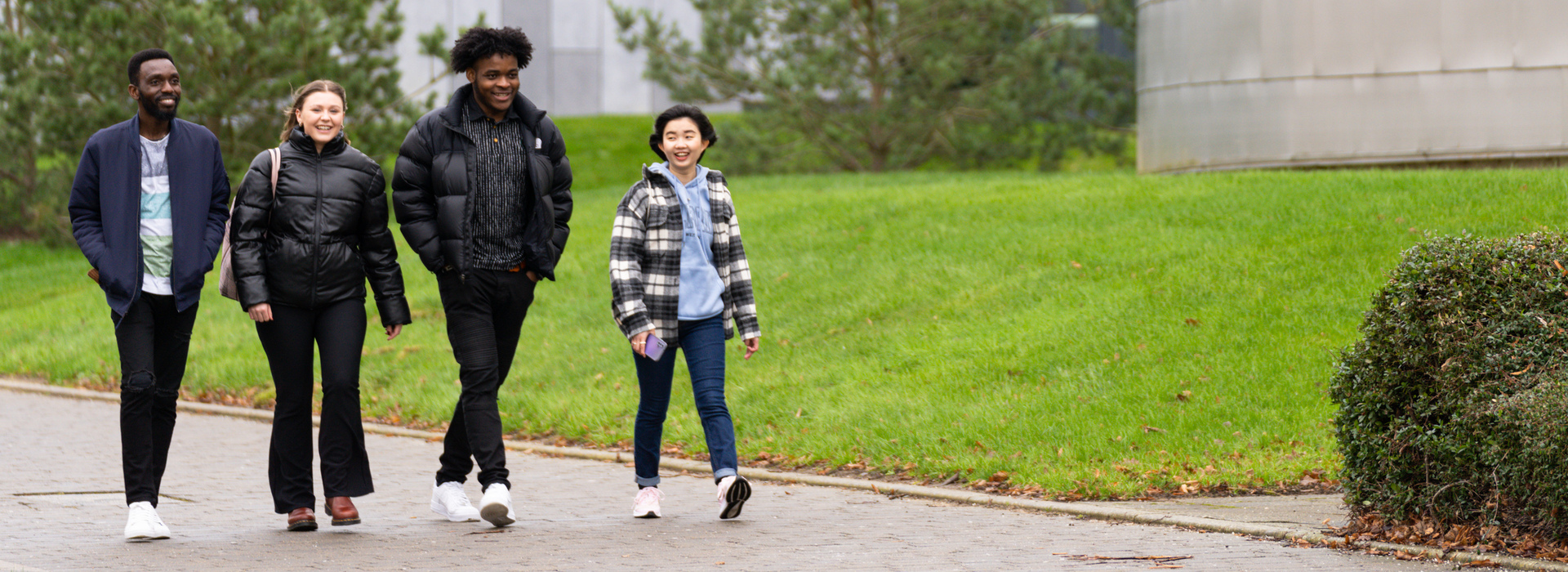  Four students from diverse backgrounds walking along campus happily together