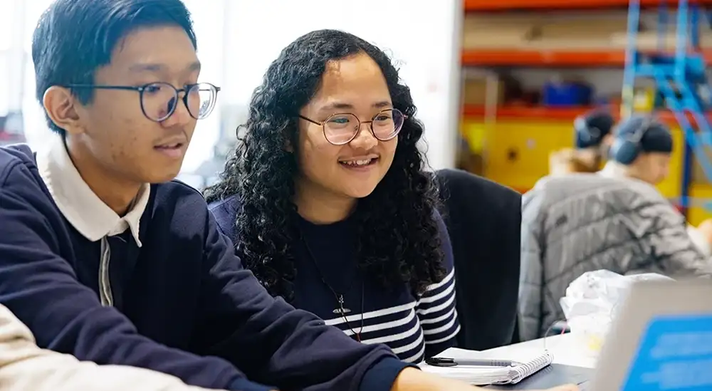 Two students looking a screen one is smiling