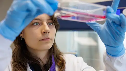 A student in a lab coat looking at a test tube