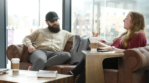 two students talk whilst sitting on a sofa