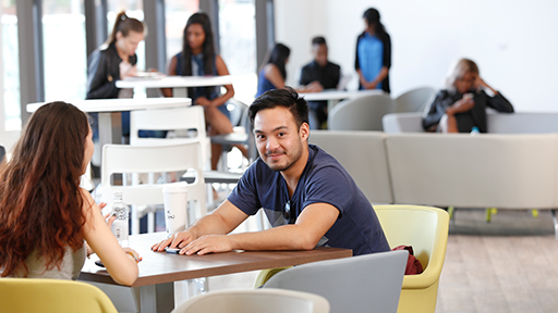 a student sits in a cafe and smiles to camera 