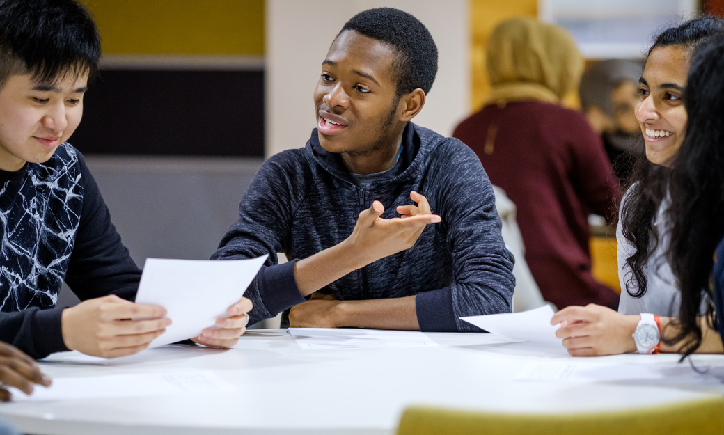 three students sitting at a table, smiling and completing a group task. 