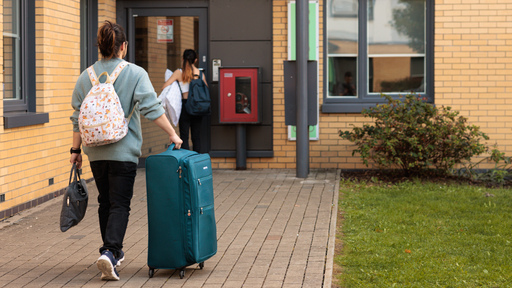 Student with wheeled suitcase, walking away