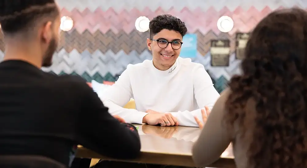A student talking to other at a table smiling at others