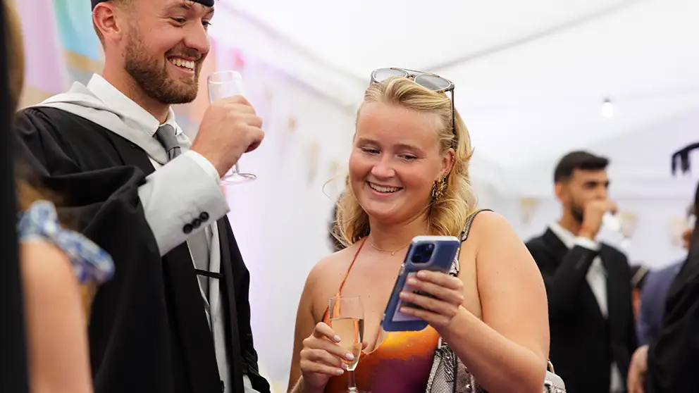 Student at graduation looking at phone 