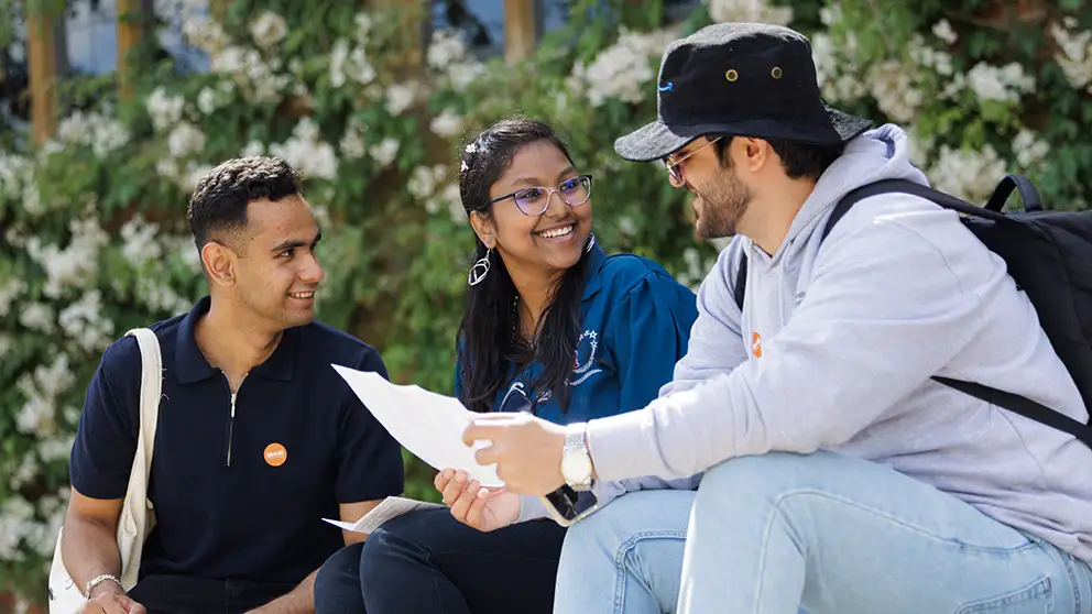 Three students sitting down talking and smiling