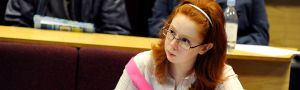 Female student wearing a pink jumper listens in a lecture theatre