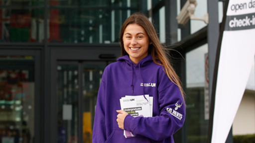 student ambassador holds leaflets and smiles