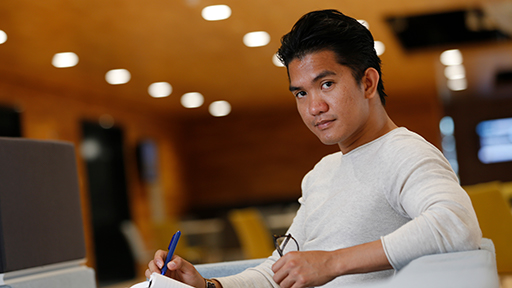 a student sits with a notepad and pen on his lap