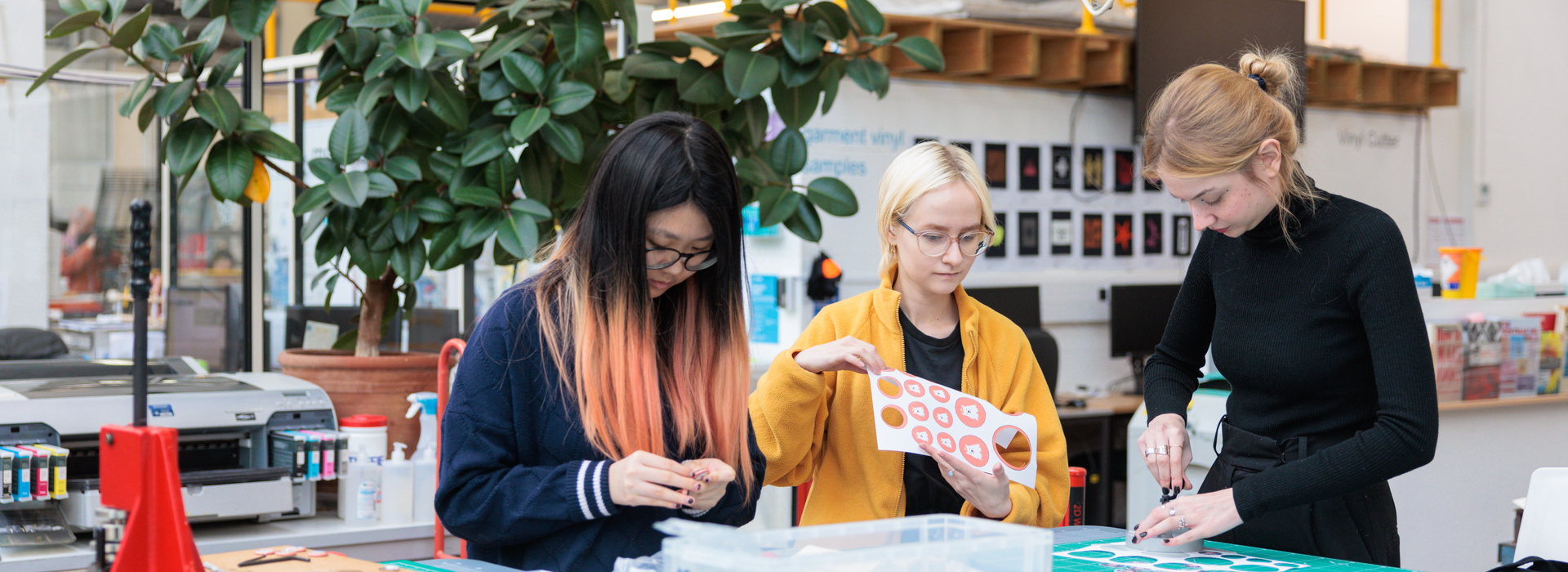 Three students standing at table, cutting stickers