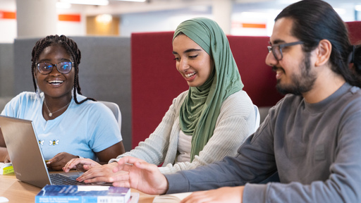 Three smiling students looking at a laptop