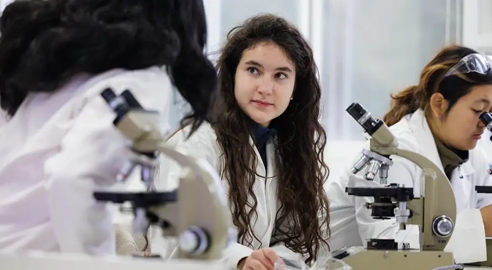 A student in a lab coat working in front of a microscope