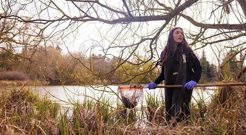 A student with a fishing net on the edge of a lake