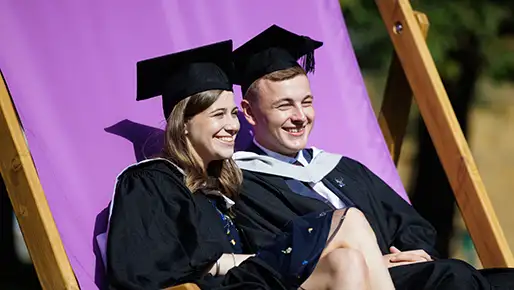 Two students at graduation taking picture while sitting